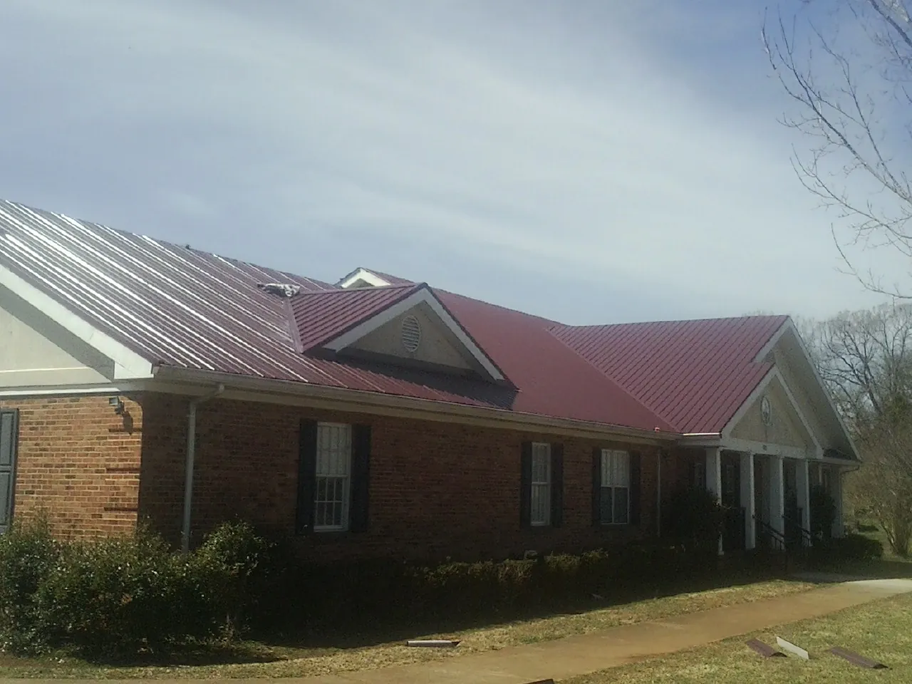 Red metal roof with gabled entries on a long brick building, from a Hail Damage Roof Repair job in Liberty Mills