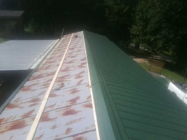 Old rusted panels beside newly installed green metal roofing — Wind Damage Roof Repair by Roofing Brothers in Liberty Mills