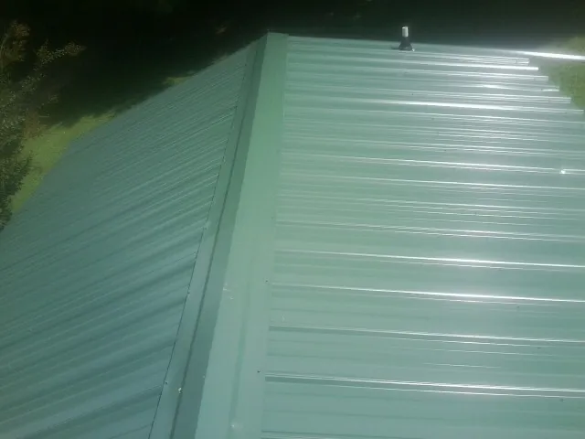 New green metal panels meeting at the ridge of a roof — Flat Roof Repair work by our crew in Liberty Mills
