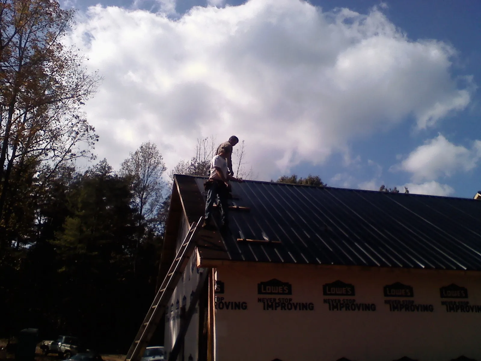 Roofer fastening dark metal panels high against a cloudy sky, from a Roof Inspection job in Liberty Mills