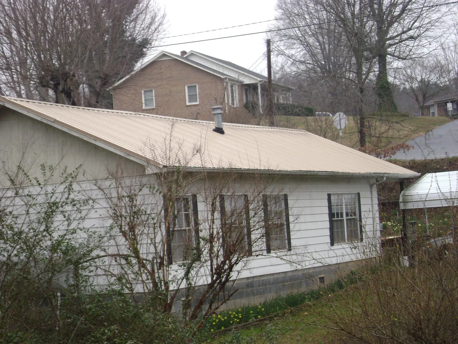 Tan metal roof on a white sided house set into a hillside — Commercial Roofing by Roofing Brothers in Liberty Mills