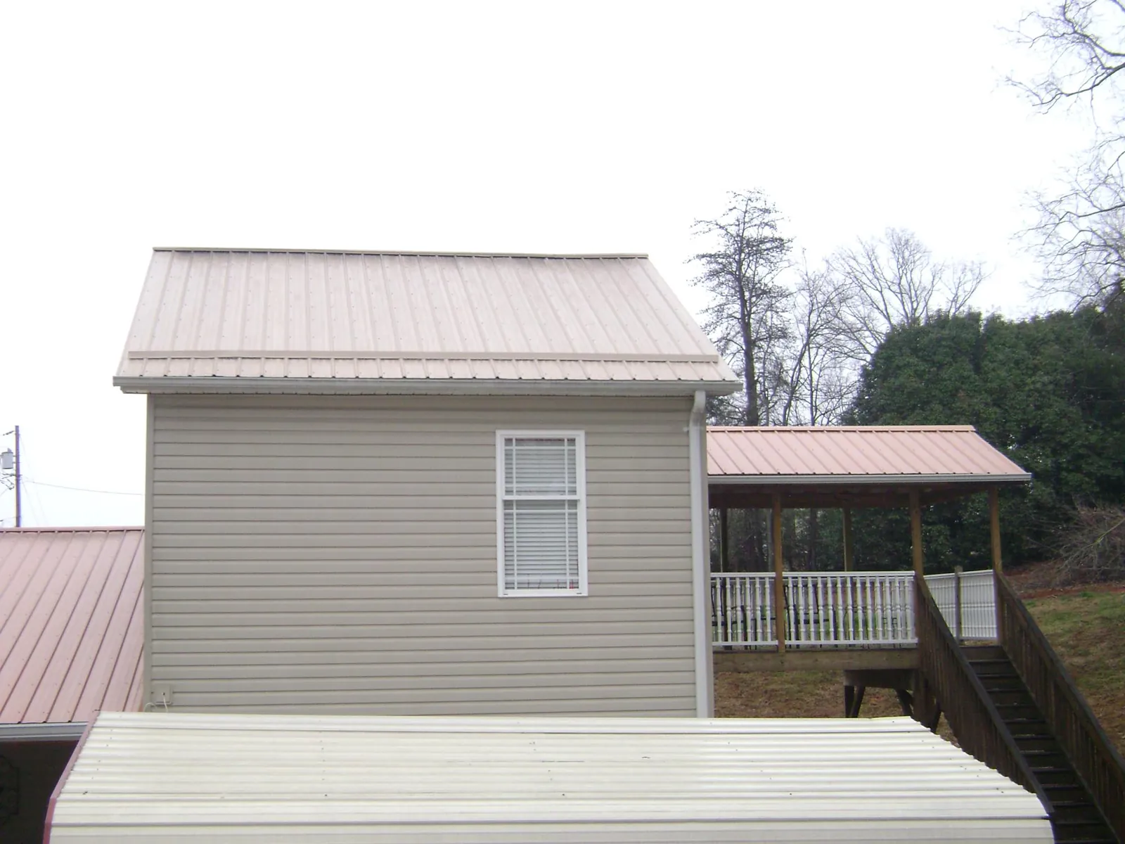 Tan metal roofs on a two story addition and attached porch, from a Roof Replacement job in Liberty Mills